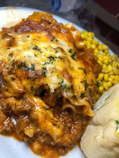 a white plate topped with lasagna, corn and mashed potatoes covered in cheese