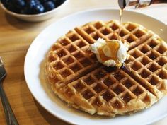 a white plate topped with waffles covered in syrup and butter next to a bowl of blueberries