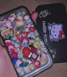 a person holding an open tin with hello kitty figurines in it's hand