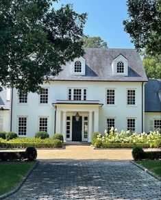 a large white house with lots of windows and bushes around it's front entrance