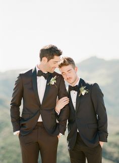 two men in tuxedos standing next to each other with mountains in the background