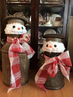 two snowmen in hats and scarfs sitting on top of a trash can next to each other