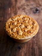 a wooden bowl filled with food sitting on top of a wooden table covered in crumbs