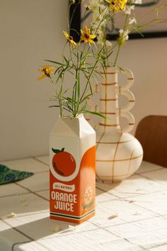 an orange juice carton sitting on top of a table with yellow flowers in it