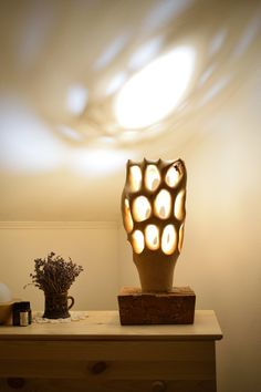 a vase sitting on top of a wooden table next to a light fixture and flowers