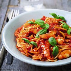 a white bowl filled with pasta covered in sauce and garnished with fresh basil