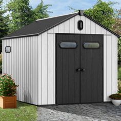 a white and black shed sitting on top of a brick walkway next to flowers in potted plants