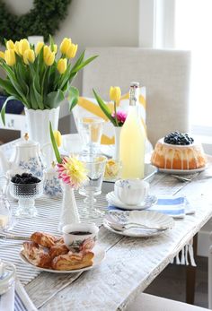 the table is set for breakfast with flowers in vases and pastries on plates