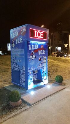 an ice machine sitting on the side of a road next to a parking lot at night