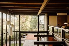 the inside of a house with glass walls and wooden ceilinging, looking out onto trees