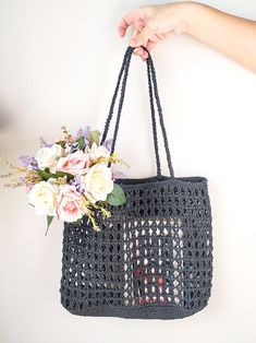 a crocheted bag with flowers in it being held by a woman's hand