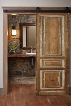 an open door leading to a bathroom with stone walls and wood floors, along with a sink