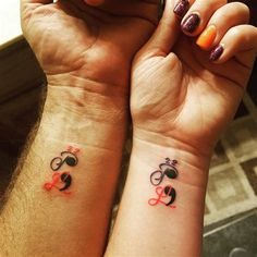 two people with matching tattoos on their wrists holding each other's hands and looking at the camera