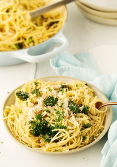 a plate of spaghetti with broccoli and parmesan cheese on top, next to a bowl of pasta