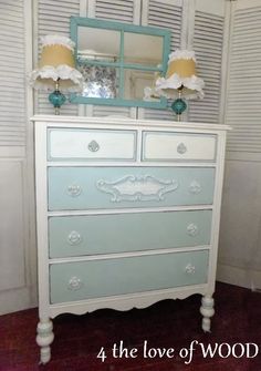 a dresser with two lamps on top of it next to a mirror and shutters