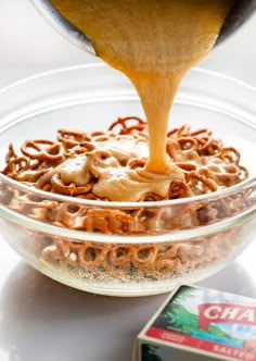 someone pouring caramel sauce on top of a bowl of cereal in a glass bowl