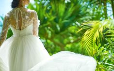 a woman in a white wedding dress is walking through the jungle with her back to the camera