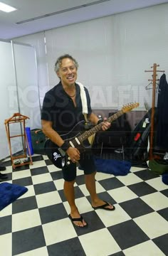 a man standing in front of a black and white checkered floor holding a guitar