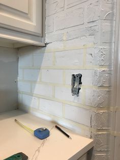 a white brick wall with some tools on the counter in front of it and an electrical outlet