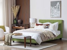 a green bed with white sheets and pillows in a room next to a chair, table and lamp