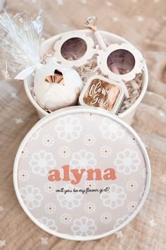 a personalized round box with sunglasses and other items in it sitting on a bed