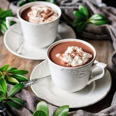 two cups of hot chocolate with marshmallows on the side and leaves around them