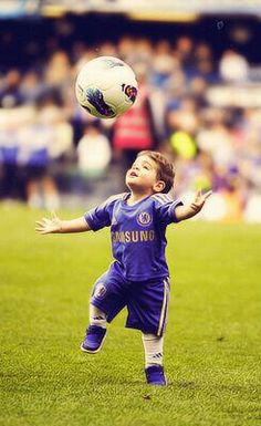 a young boy playing with a soccer ball on a field in front of an audience