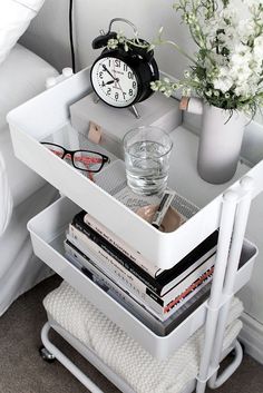 a nightstand with a clock, glasses and flowers on it