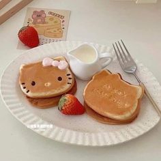 a white plate topped with two pancakes covered in hello kitty toppings next to a cup of coffee