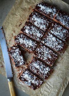 chocolate brownies with powdered sugar on top, cut into squares and sitting next to a knife