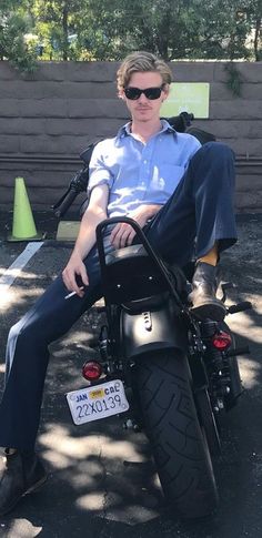 a man sitting on top of a motorcycle in the shade with his feet propped up