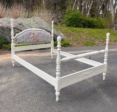 a white bed frame sitting on top of a parking lot next to a large rock