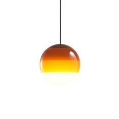 an orange and yellow light hanging from a black cord on a white background with the sun reflecting off it's side