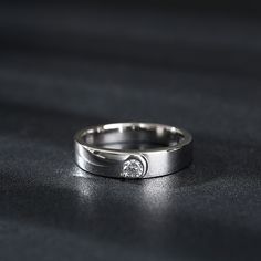 a white gold wedding band with a single diamond in the center on a black surface