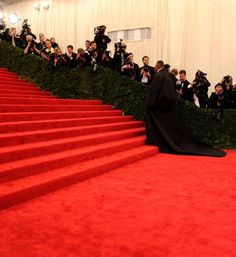 a woman in a black gown is walking down the red carpeted stairs with cameras around her