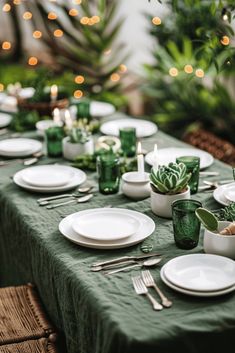 the table is set with white plates and green napkins, candles and succulents