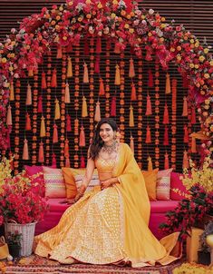 a woman sitting on top of a pink couch in front of a flower covered wall