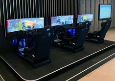 three computer monitors sitting next to each other on a black table with video game controllers in front of them