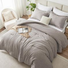 a bed with grey comforter and pillows in a room next to a white chair