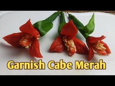 three red flowers with green leaves on top of a white plate that says, garnish cabe merah