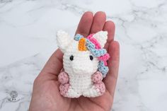 a small crocheted stuffed animal in someone's hand on a marble surface