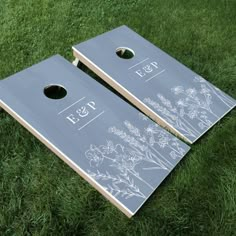 two cornhole game boards sitting on top of green grass with white flowers painted on them