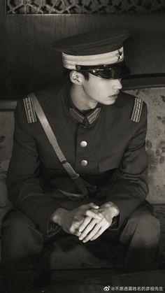 a black and white photo of a man in uniform sitting on a couch with his hands folded