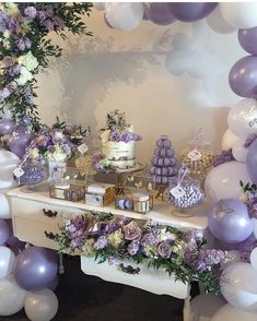 a table with purple and white balloons, cake and flowers on it in front of a mirror