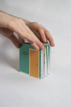 a person holding an open book in their hand on a white surface with one hand