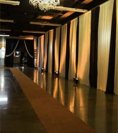 a long hallway with black curtains and a chandelier hanging from it's ceiling