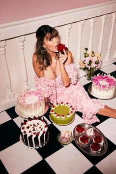 a woman in pink dress sitting on floor next to cakes