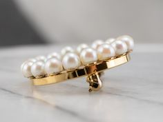 This vintage pearl circle brooch is a true classic! Simple and refined, traditional white pearls form a shimmering wreath, backed by rich yellow gold. This brooch would look wonderful pinned to a scarf or lapel, or even on a bridal bouquet! Love this piece but want to make it more versatile? We here at Market Square Jewelers, along with our master metalsmiths can convert this fantastic brooch into a necklace or pendant for an additional fee. Please contact us for more information! Metal: 10K Yel Classic Yellow Gold Brooches For Wedding, Classic Yellow Gold Wedding Brooches, Timeless Wedding Brooch Jewelry, Classic Round Yellow Gold Brooches, Classic Yellow Gold Round Brooches, Classic Gold Round Brooches, Gold Brooch With Pearl Pendant For Wedding, Gold Wedding Brooch With Pearl Pendant, Jewelry Bouquet