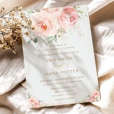 the wedding card is laying on top of some white sheets with pink flowers and greenery