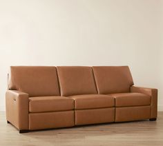 a brown leather couch sitting on top of a hard wood floor next to a white wall